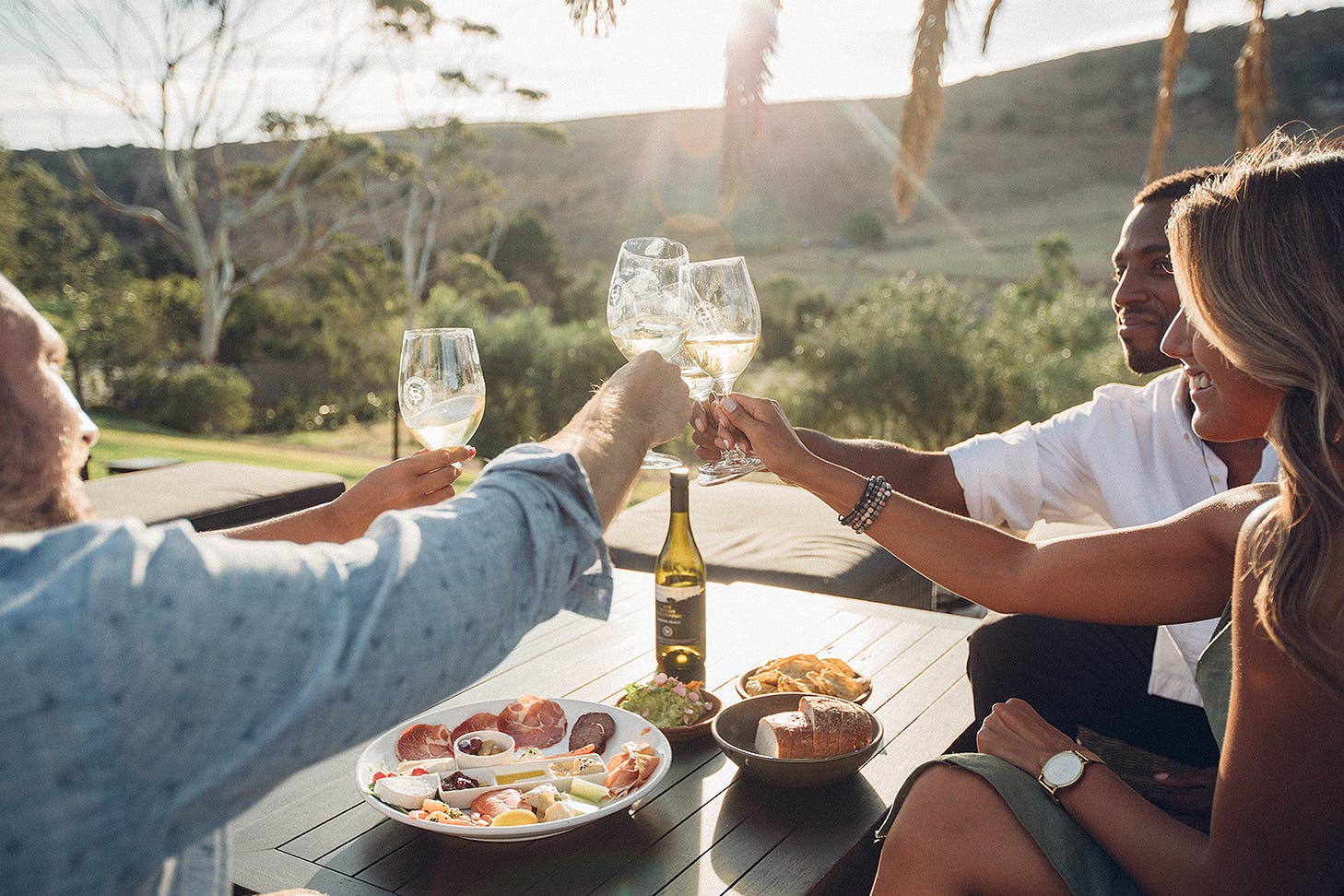 Friends clinking glasses of wine while sitting outside at Stonyridge vineyard on Waiheke